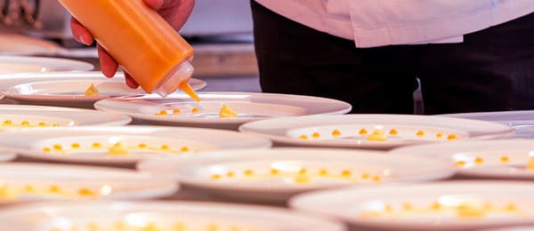 Eine Person richtet Teller an mit gelber Sauce